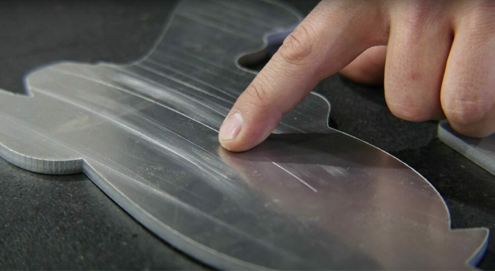 Screenshot from the video showing Jake pointing to surface scratches left on a sheet metal part prior to deburring.