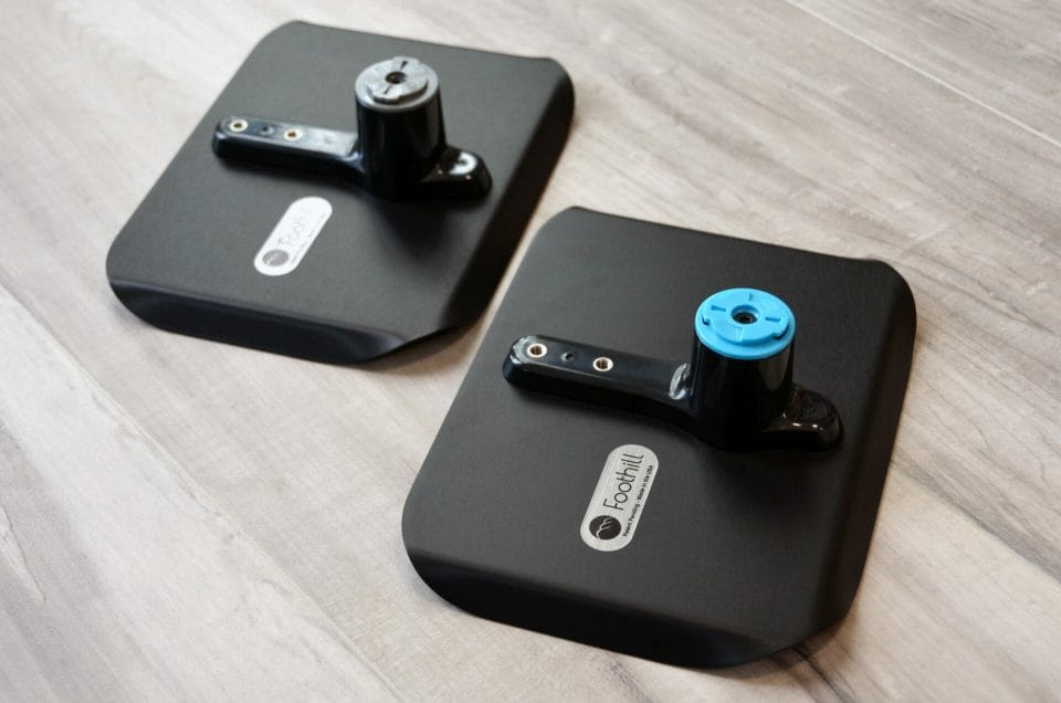 Two black anodized aluminum mount trays from Foothill products sitting face down on a wood floor, showing the Foothill logo etched into the bottom.