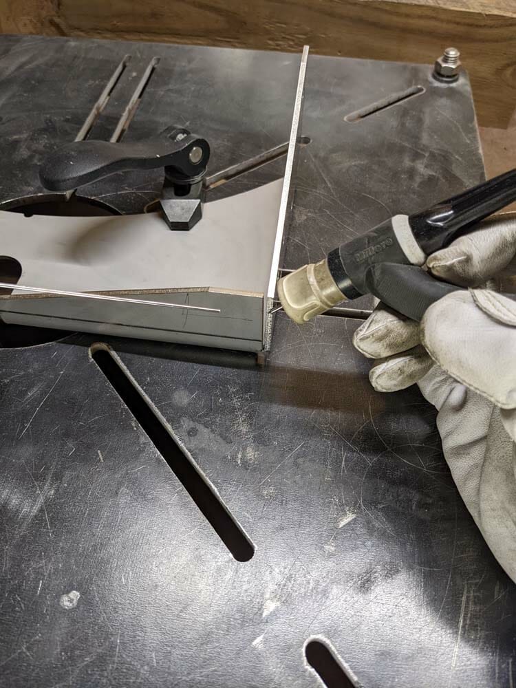 Image of someone holding a tig welding torch to the fitted corners of two laser cut aluminum parts.