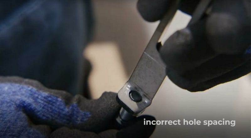 Screenshot from the video showing a bent part with a hole too close to the die line and the hole is warped with a poorly fitting screw inside of it. It's denoted with "incorrect hole spacing" written in the bottom right corner