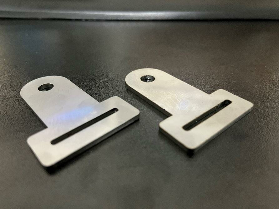 Image of two of the real brackets, laser cut out of aluminum and sitting on a steel table