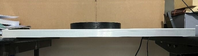 1 black weight resting on the center of the sheet metal part, with no deformation, demonstrating bending stiffness.