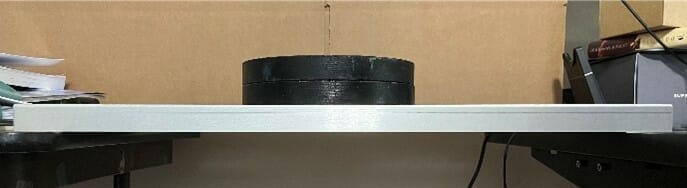 2 black weights resting on the center of the sheet metal part, with no deformation, demonstrating bending stiffness.