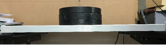 3 black weights resting on the center of the sheet metal part, with no deformation, demonstrating bending stiffness.