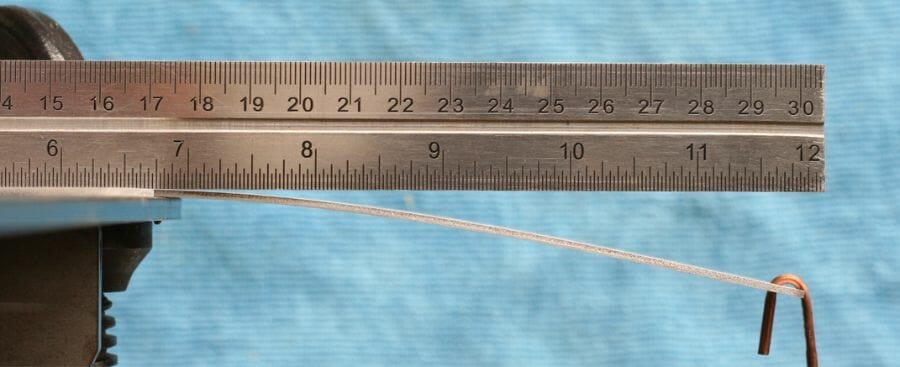 Image of a flat part being bent by a downward force with a ruler above it for comparison