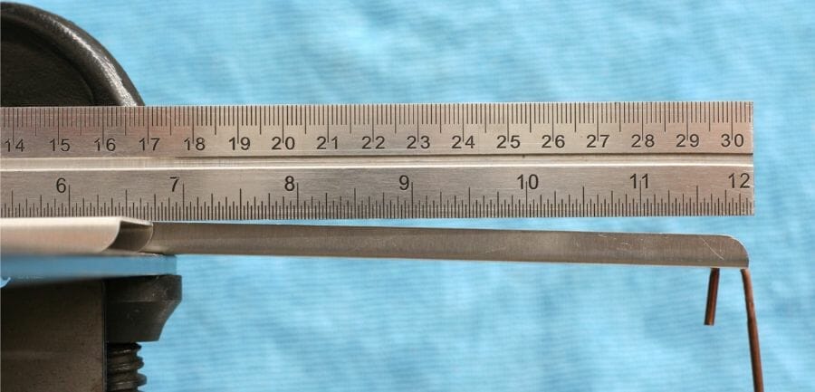 Image of the thin rectangular sheet metal part from the previous image being bent with a downward force with a ruler above it for comparison. There is little deformation thanks to the flanges