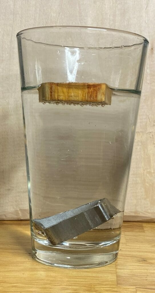 A piece of steel and a piece of pine in a glass of water to demonstrate object density